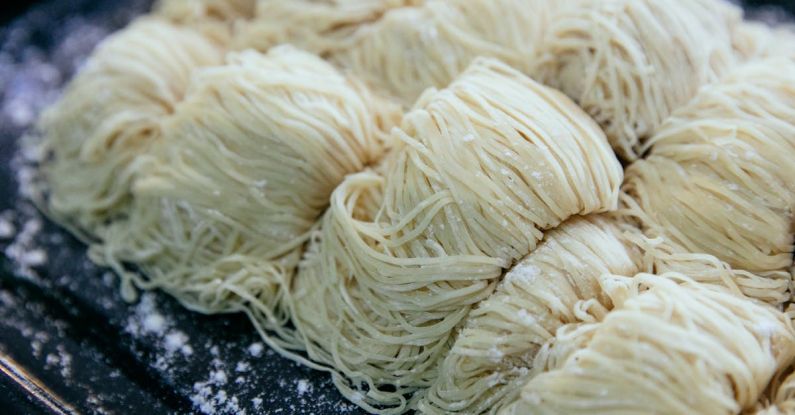 Pasta - Homemade egg noodles collected in rolls and sprinkled with flour on black baking sheet