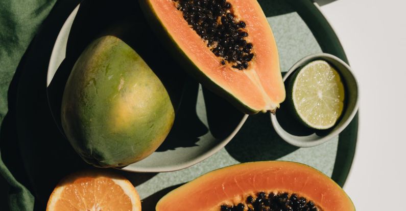 Vegetarian Diet - Top view of halves of ripe papaya together with oranges and limes placed on green round dishes and green fabric on white background